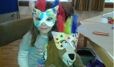 Ein Kind und ein Kuscheltier haben selbst gebastelte Masken auf