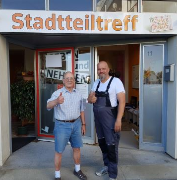 Zwei Handwerker vor dem neuen Stadtteiltreff-Schild